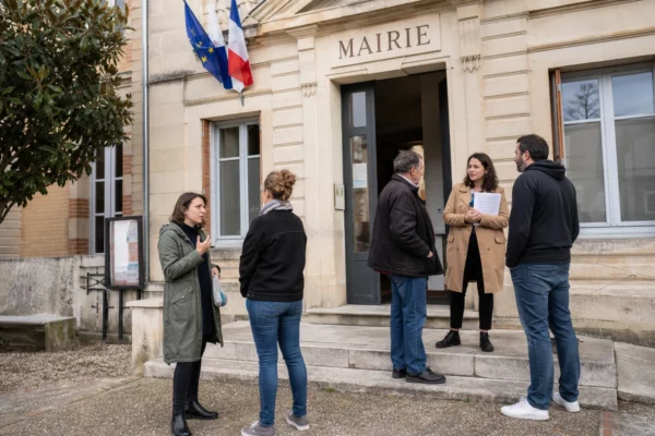 Des habitants discutent devant la mairie d’une petite ville, dans une scène de proximité civique en lumière naturelle.