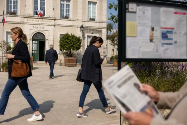 Des passants anonymes devant une mairie française, avec notice floue et journal plié, dans une ambiance civique calme.
