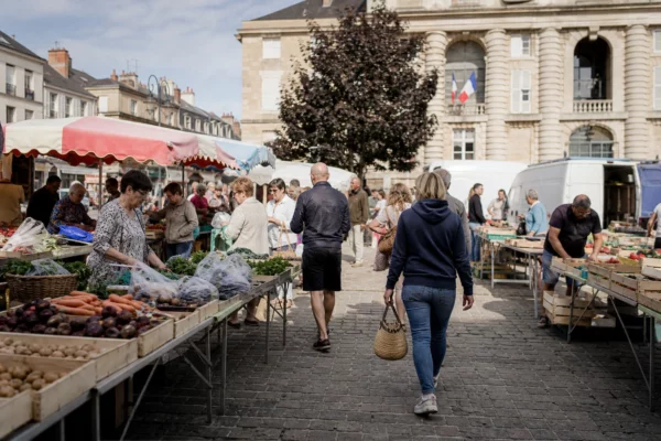 Marché de La Flèche en Sarthe, avec des habitants anonymes et des étals de produits sous la lumière du matin.