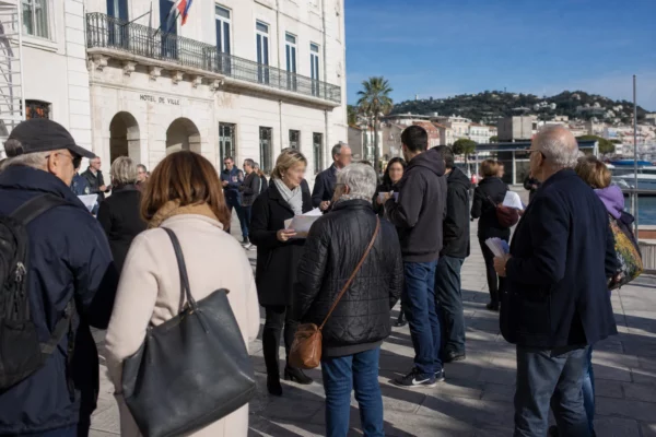 Scène de campagne politique sur une place côtière française, avec passants anonymes et ambiance de meeting local.