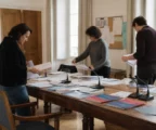 Salle municipale lumineuse à Erfurt avec micros, dossiers flous et chaise vide avant une mobilisation contre l’AfD.