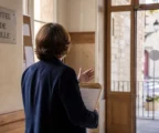 Un élu local de dos consulte un dossier dans une mairie française, sur fond de rue floue et lumière naturelle.