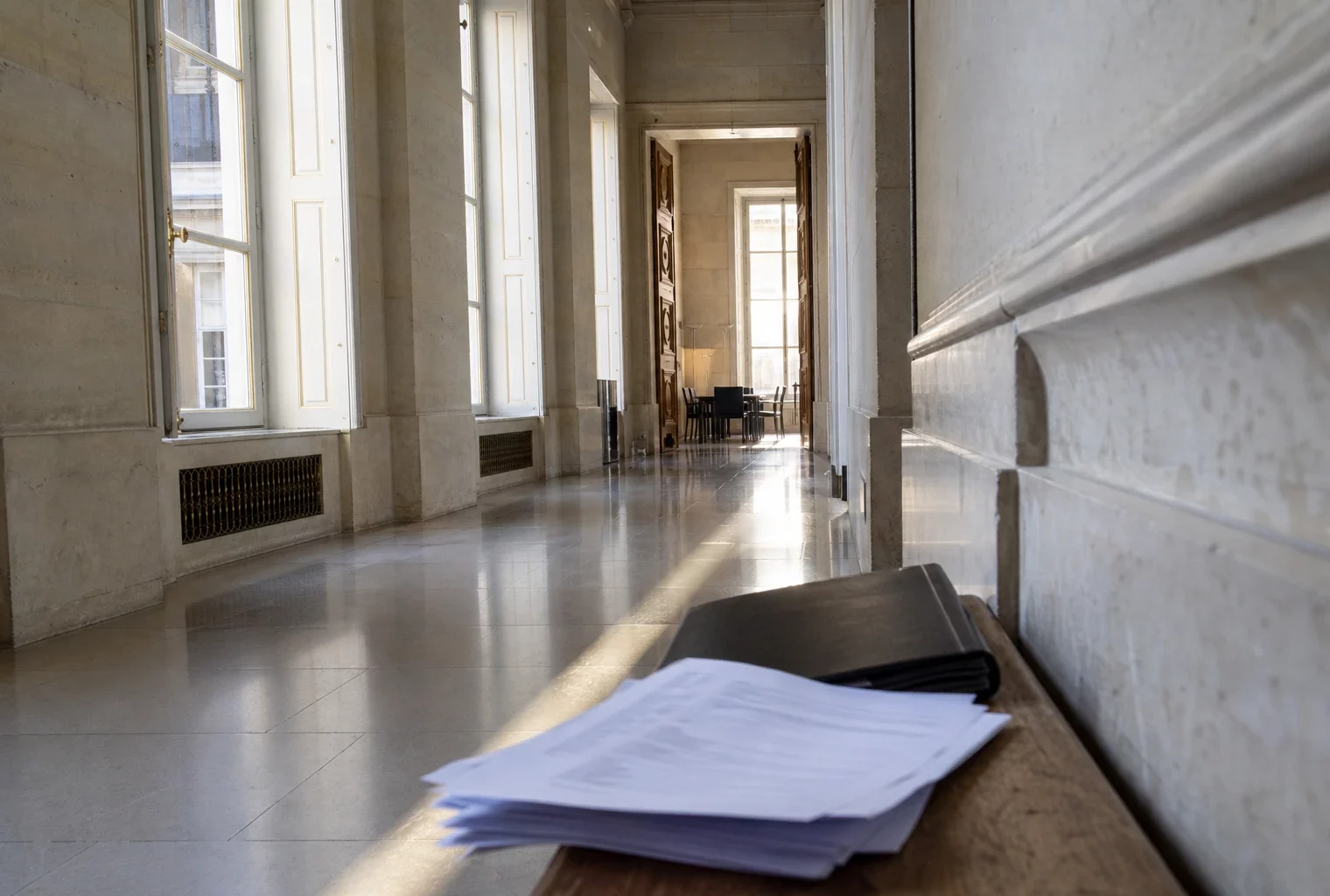 Couloir vide de l’Assemblée nationale avec dossiers flous, lumière naturelle et atmosphère de tension parlementaire.