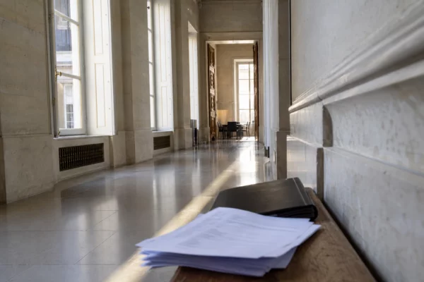 Couloir vide de l’Assemblée nationale avec dossiers flous, lumière naturelle et atmosphère de tension parlementaire.