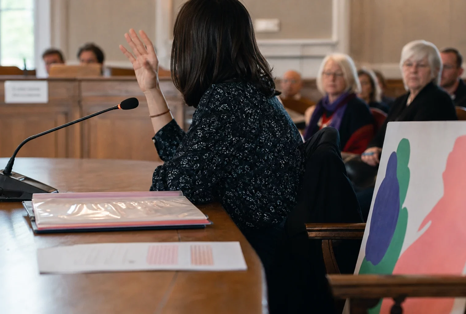 Salle publique française avec micro, document juridique flou et personne levant la main lors d’un débat institutionnel.