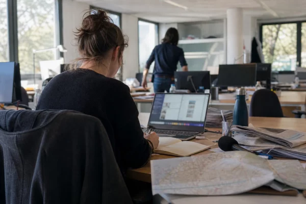 Journaliste en rédaction préparant un sujet territorial sur la canicule, avec carnet, micro et carte floue.