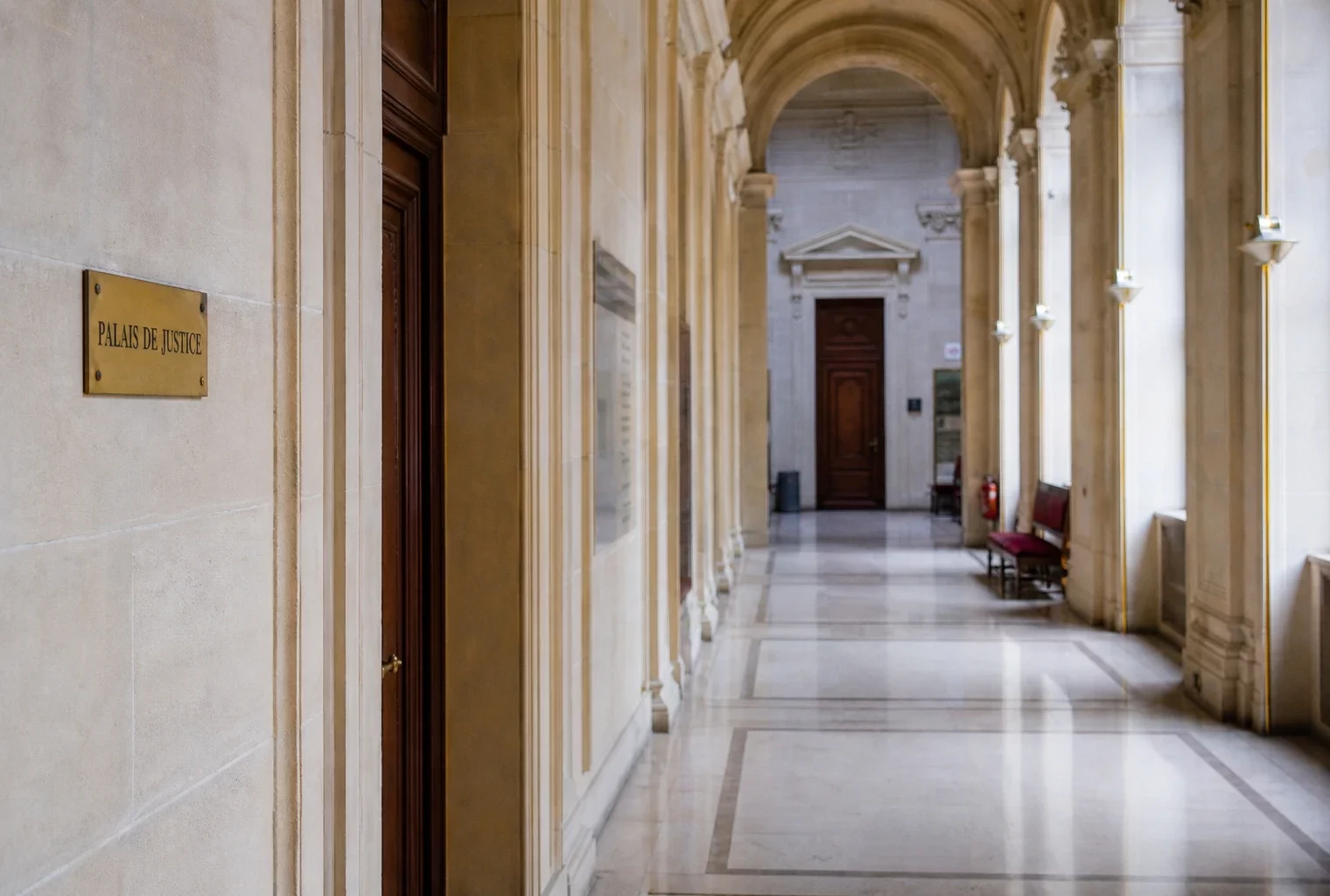 Couloir lumineux du Palais de justice à Paris, avec marbre clair et plaque institutionnelle discrète.