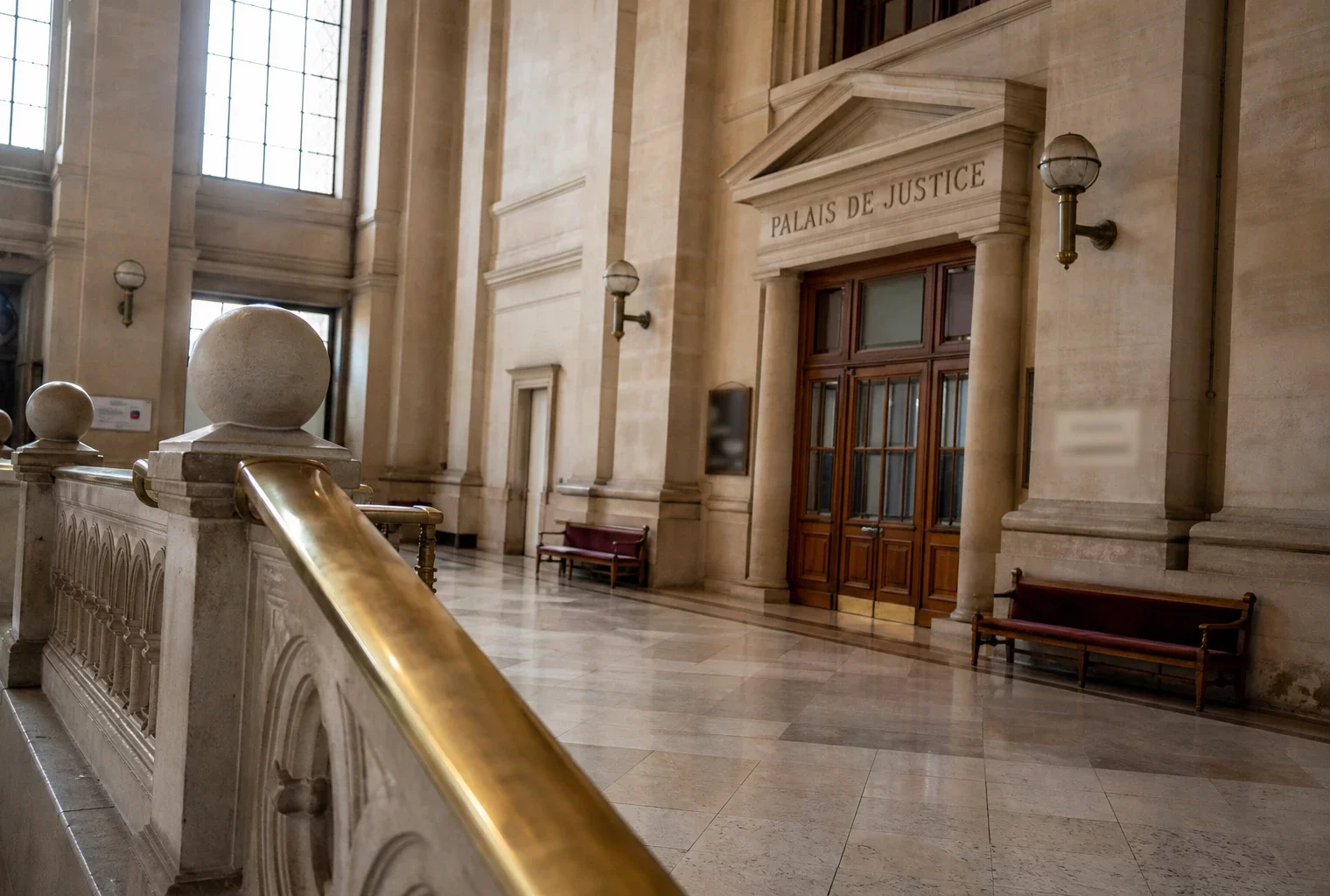 Intérieur lumineux du palais de justice, couloir vide en pierre et marbre avec signalétique institutionnelle discrète.