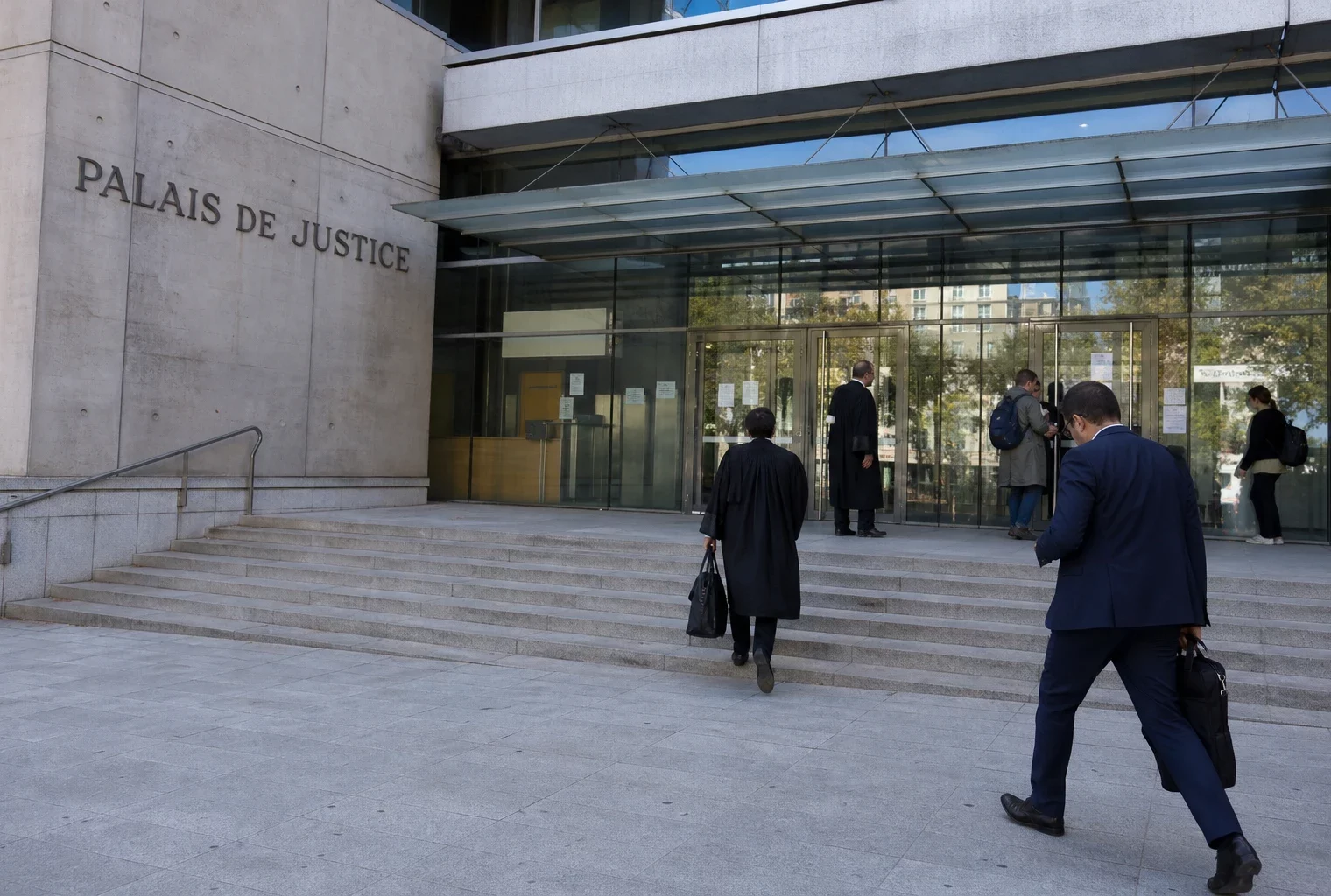 Devant le palais de justice de Paris, journalistes et avocats se croisent dans une scène documentaire en journée.
