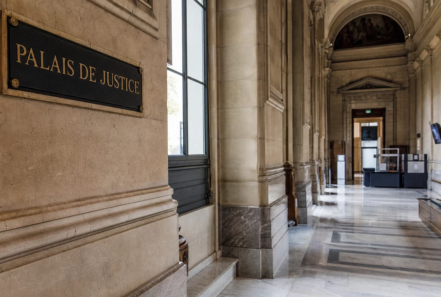 Couloir lumineux du palais de justice de Paris, vide, avec marbre clair et signalétique institutionnelle discrète.