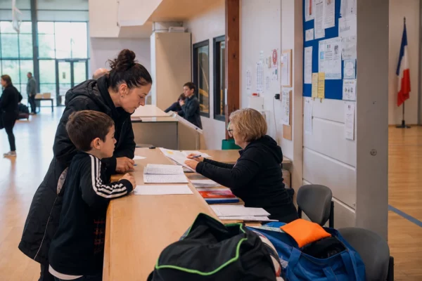 Des parents inscrivent leur enfant dans un club de sport, dans un hall lumineux de mairie, avec un bénévole au comptoir.