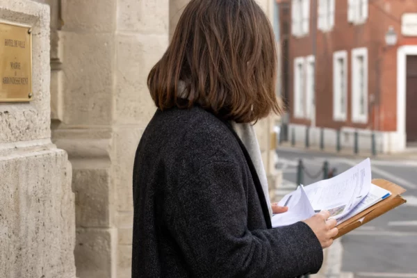 Un collaborateur de mairie vu de dos consulte un dossier devant une façade de mairie française