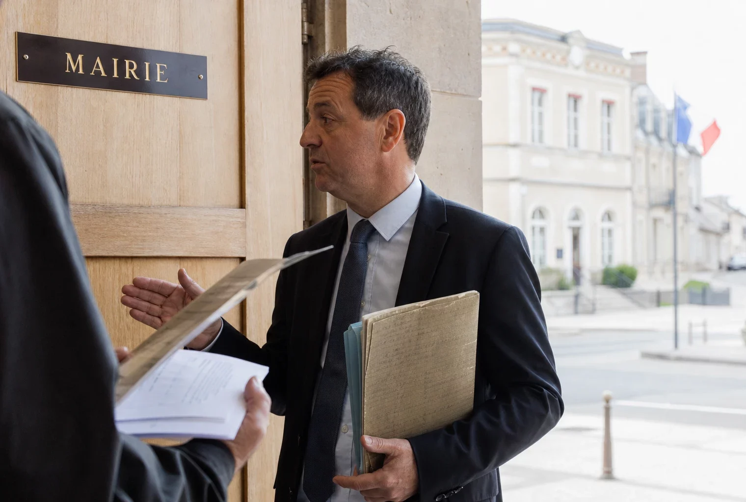 Un élu local anonyme consulte un dossier dans un couloir de mairie, en lumière naturelle et ambiance de reportage.