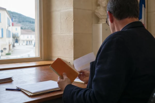 Un élu local de dos consulte un dossier dans une mairie française lumineuse, en arrière-plan une rue calme.