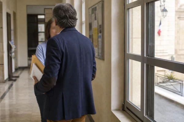 Élu local anonyme dans un couloir de mairie, tenant un dossier, avec une rue française en arrière-plan.