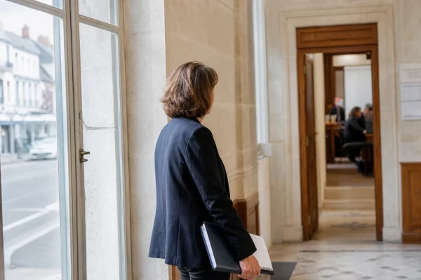 Élue locale anonyme de dos dans un couloir de mairie, carnet et dossier à la main, en lumière naturelle.