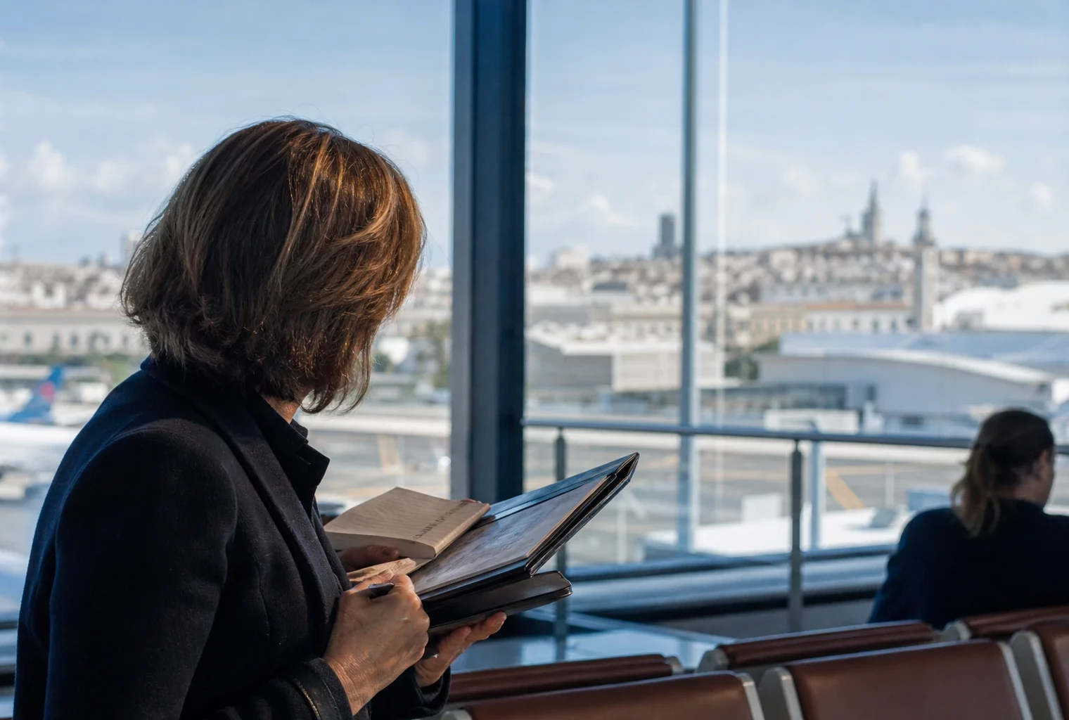 Élu local anonyme tenant un carnet dans un terminal, avec arrière-plan urbain français flou et lumière naturelle.