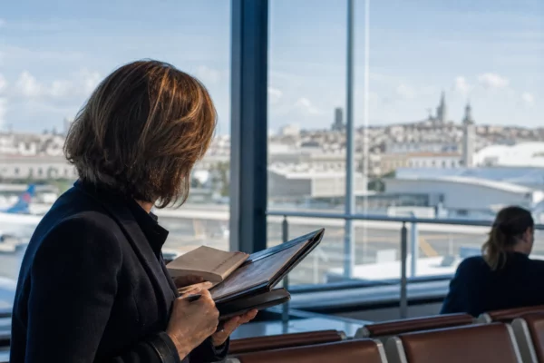 Élu local anonyme tenant un carnet dans un terminal, avec arrière-plan urbain français flou et lumière naturelle.