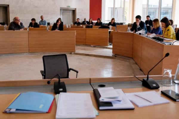 Salle municipale française lumineuse avec chaise vide, micros et dossiers flous, ambiance de réunion politique locale