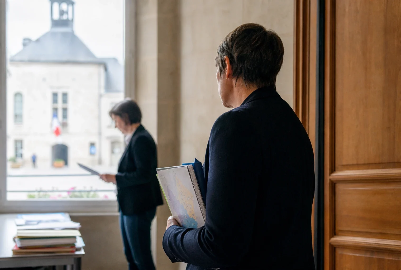 Portrait photojournalistique d’un élu local anonyme dans un couloir de mairie avec dossier et carnet à la main.