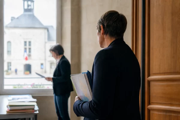 Portrait photojournalistique d’un élu local anonyme dans un couloir de mairie avec dossier et carnet à la main.