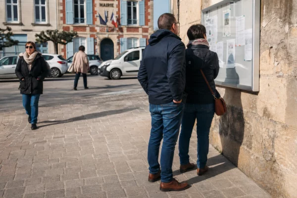 Des habitants marchent sur une place de mairie de ville moyenne, dans une scène civique calme et lumineuse.