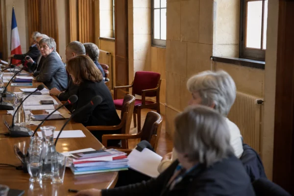 Salle municipale française avec micros, dossiers et une chaise vide lors d’une réunion politique locale
