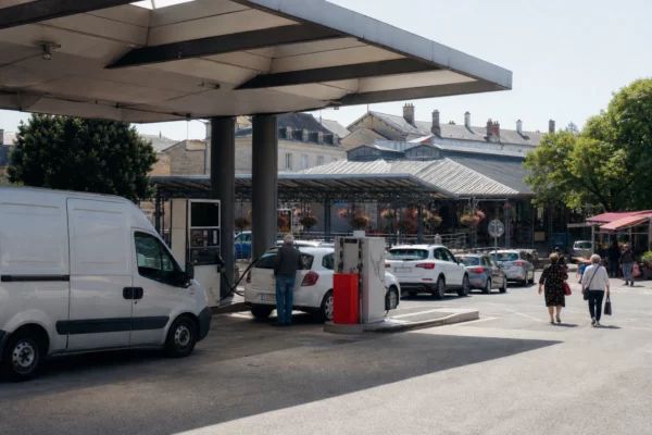 Reportage dans une ville française, devant une station-service générique avec des automobilistes et passants anonymes.