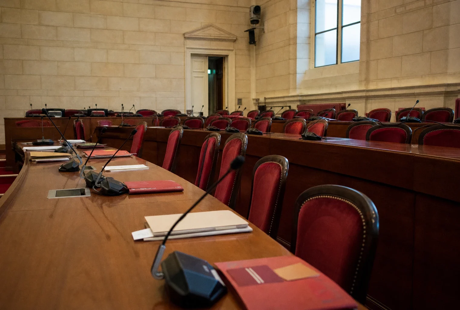 Salle de commission du Sénat avec micros et dossiers flous sous une lumière naturelle claire.