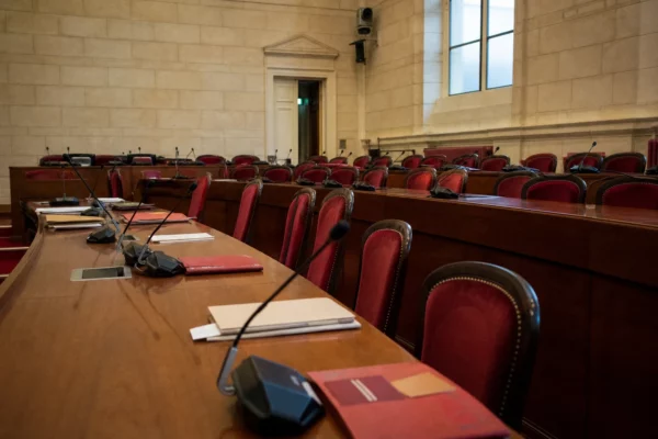 Salle de commission du Sénat avec micros et dossiers flous sous une lumière naturelle claire.