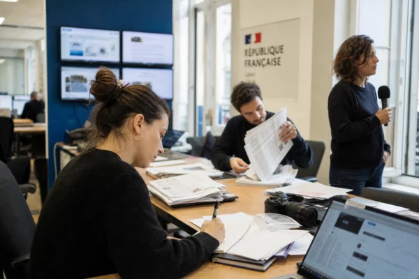 Rédaction française en pleine préparation d’un sujet politique, avec documents flous, micro et écrans abstraits.