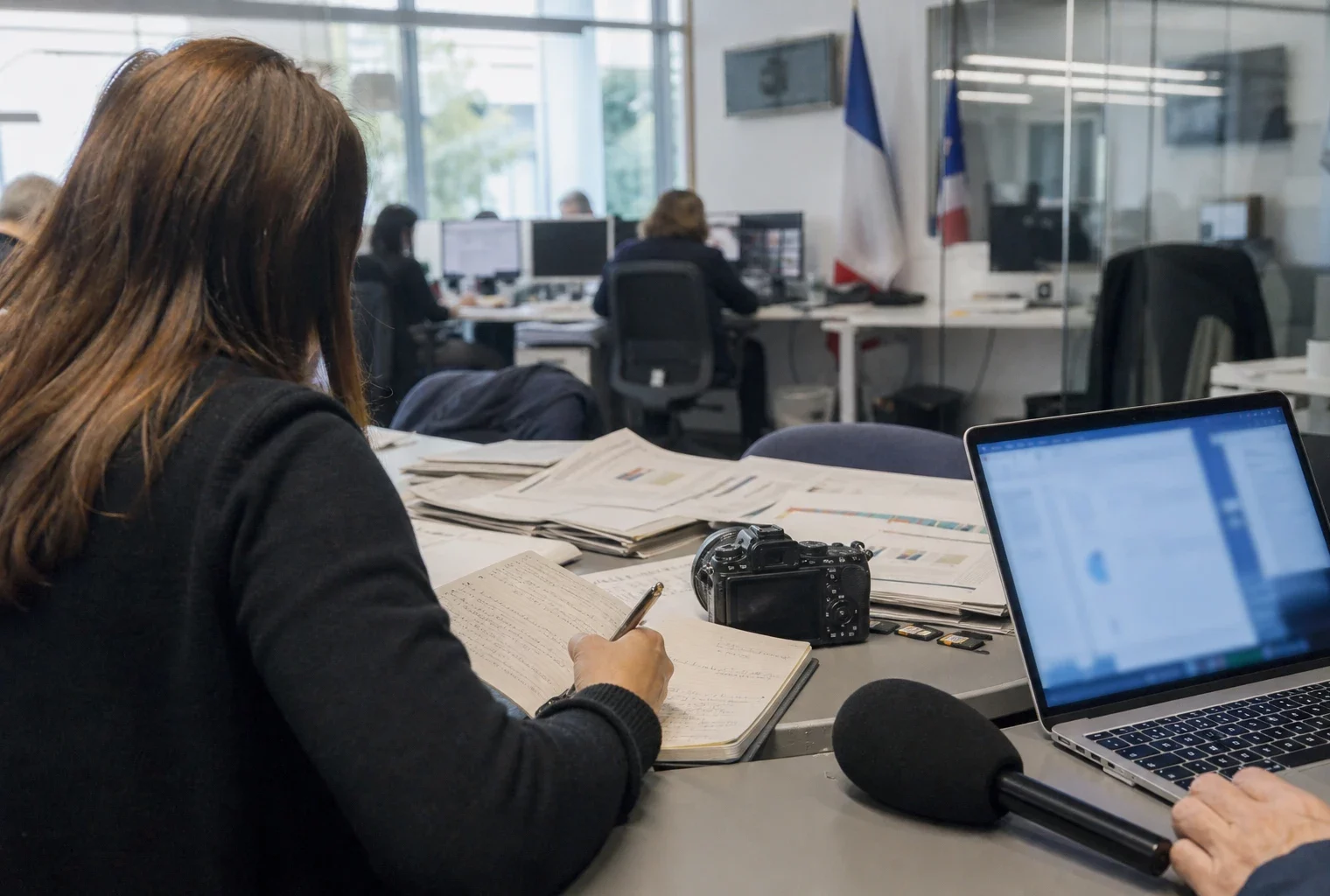 Journalistes dans une rédaction française, avec micro, carnet et écrans flous, en préparation d’un sujet politique.