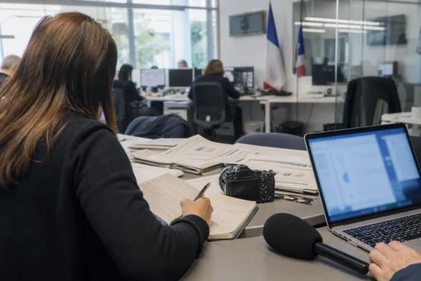 Journalistes dans une rédaction française, avec micro, carnet et écrans flous, en préparation d’un sujet politique.