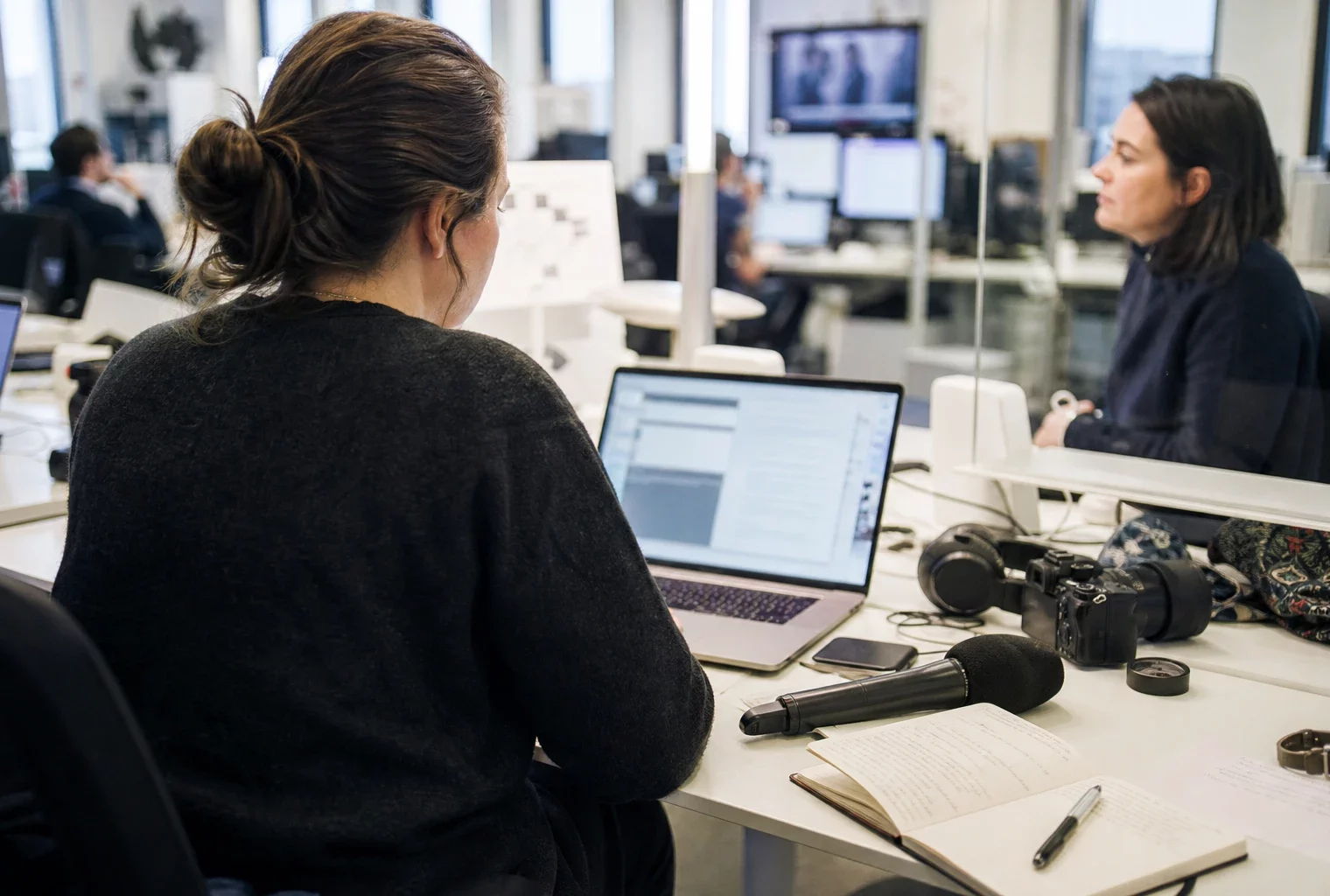 Rédaction française lumineuse avec journaliste de dos, micro sans logo et écran abstrait pour un sujet politique.