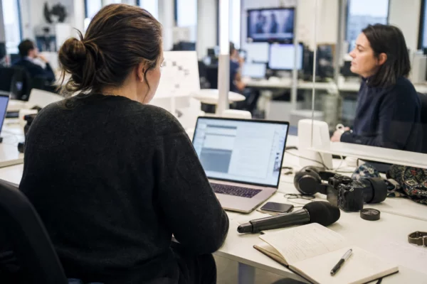 Rédaction française lumineuse avec journaliste de dos, micro sans logo et écran abstrait pour un sujet politique.