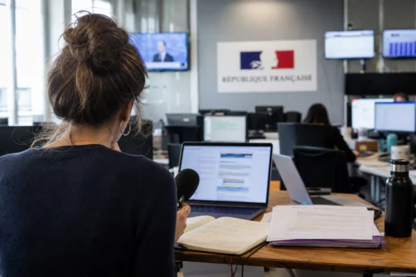 Journaliste dans une rédaction française préparant un sujet sur Sciences Po et ESCP, avec micro, carnet et écrans flous.