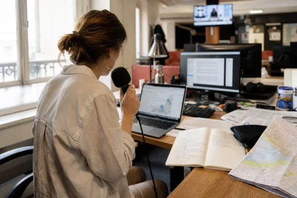 Journaliste en rédaction préparant un sujet sur les feux de forêt, avec micro, carnet et écran floutés.