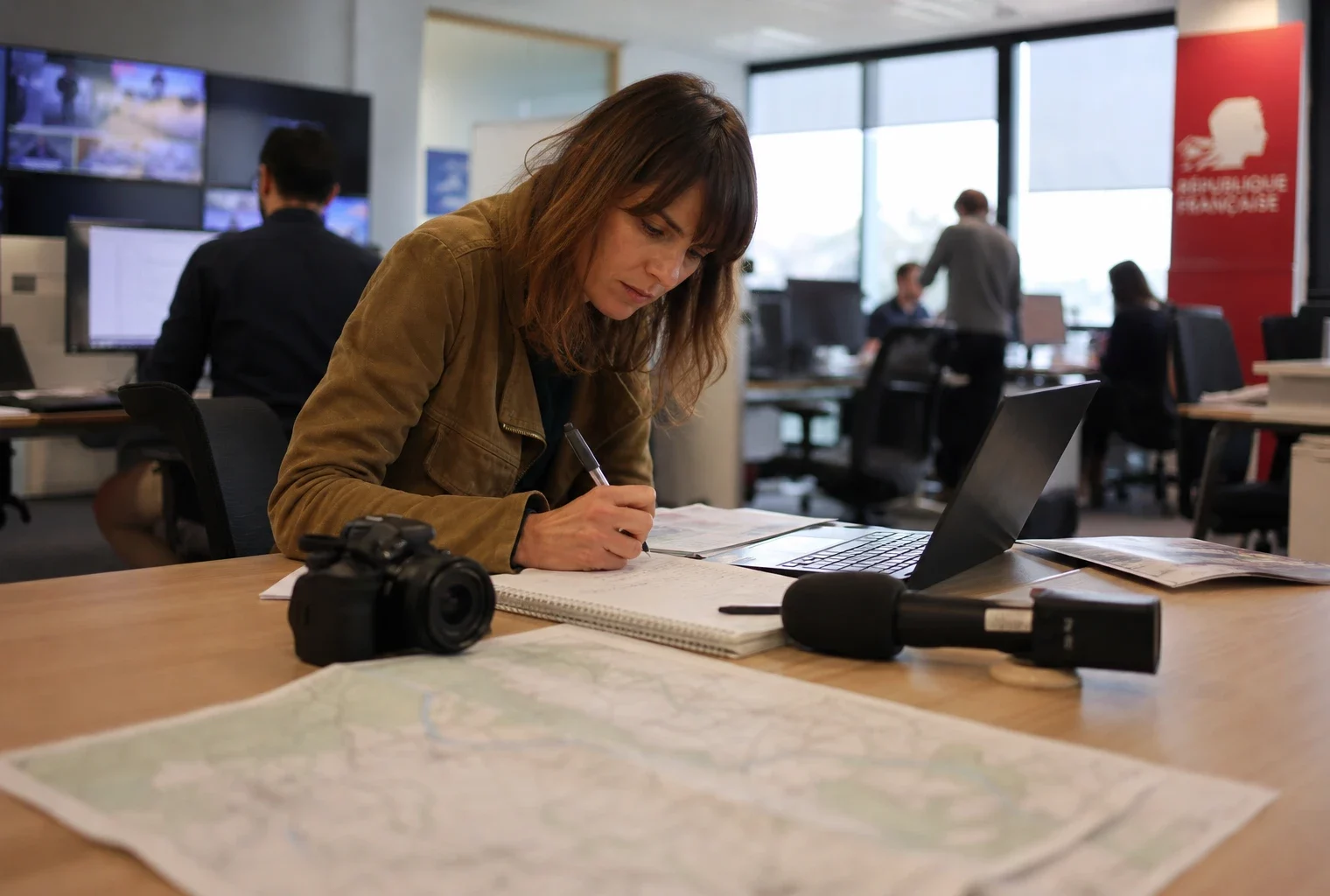 Journaliste en rédaction préparant un sujet sur les incendies en Gironde, avec carnet, micro et écrans flous.