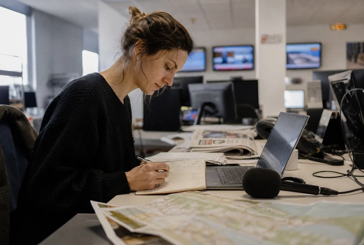 Journaliste en rédaction préparant un sujet sur les feux de forêt, avec micro, carnet et carte floue.