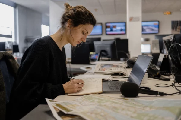 Journaliste en rédaction préparant un sujet sur les feux de forêt, avec micro, carnet et carte floue.