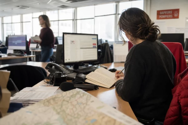 Journaliste en rédaction préparant un sujet territorial sur les incendies, avec carnet, micro et carte floue.