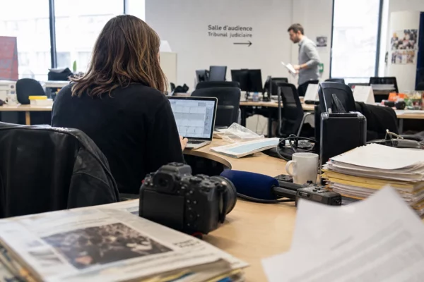 Journaliste dans une rédaction française avec caméra, micro et documents de tribunal flous