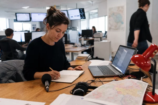 Journaliste en rédaction préparant un sujet sur les incendies et le Tour de France, avec carnet, carte floue et micro sans logo.