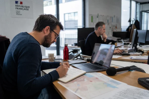 Journaliste en rédaction préparant un sujet territorial avec carnet, micro sans logo et carte papier floue