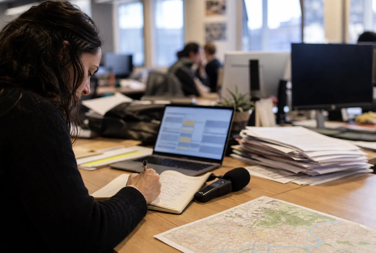 Journaliste en rédaction locale à Lyon, préparant un sujet politique avec carnet, micro sans logo et carte floue.
