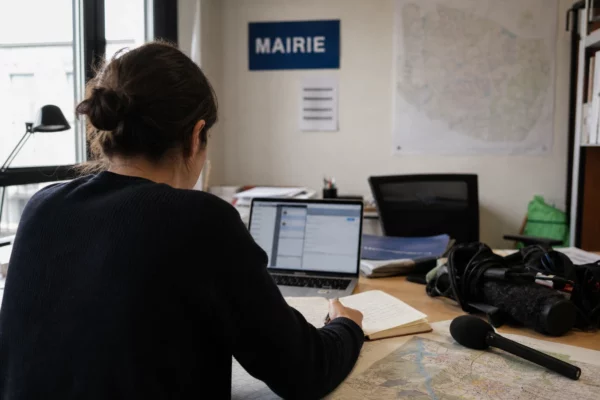 Journaliste en rédaction préparant un sujet territorial avec carnet, micro et carte floue de Seine-Saint-Denis