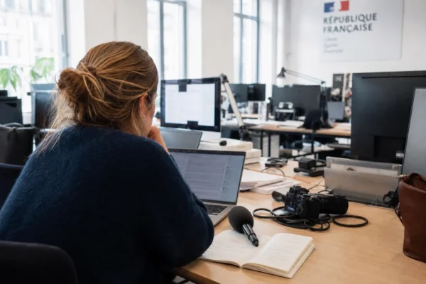 Journaliste dans une rédaction française, avec micro, carnet et écrans flous pour un sujet politique sur l’aide à mourir