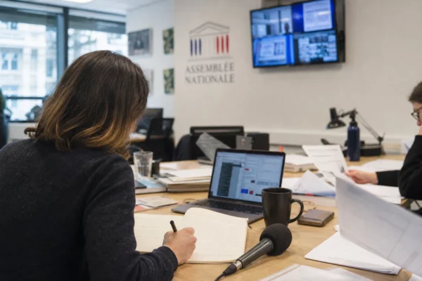 Journaliste en rédaction préparant un sujet sur la fin de vie, avec micro, carnet et écrans flous.