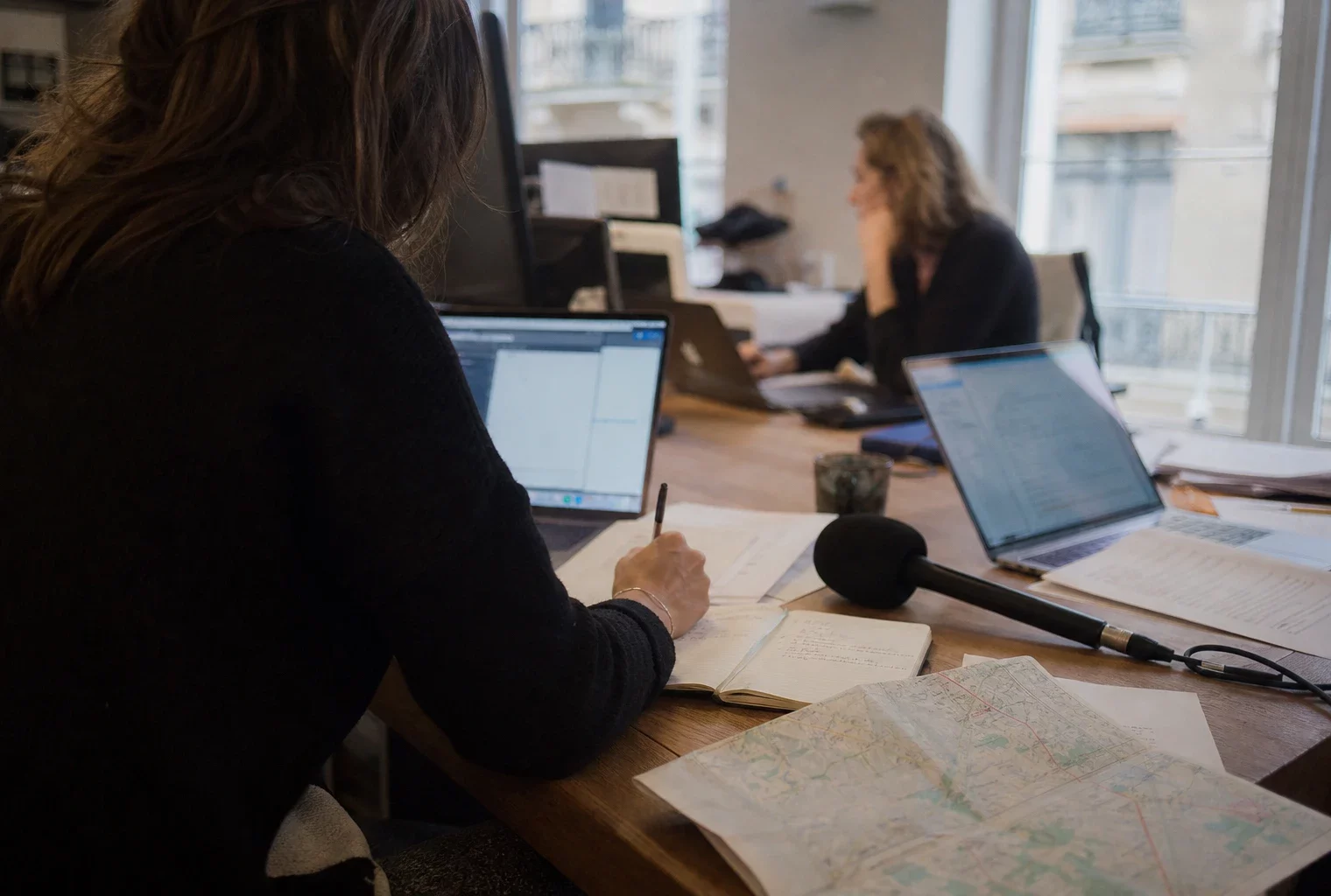 Journaliste préparant un sujet sur la fin de vie dans une rédaction française lumineuse, avec micro, carnet et écrans flous.