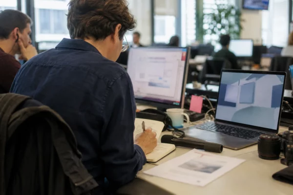Dans une rédaction française, un journaliste prépare un sujet politique avec micro, carnet et écrans flous.